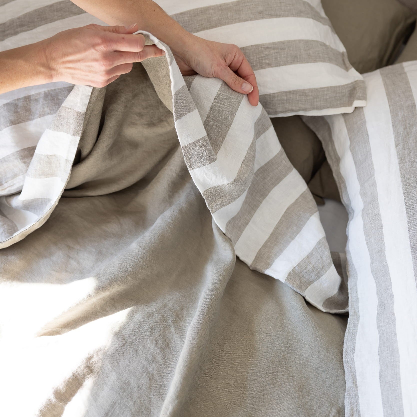 Hands showing the reversible nature of a linen duvet cover, moss green and ivory, plain moss on one side, moss and ivory stripe on the other side 
