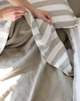 Hands showing the reversible nature of a linen duvet cover, moss green and ivory, plain moss on one side, moss and ivory stripe on the other side 
